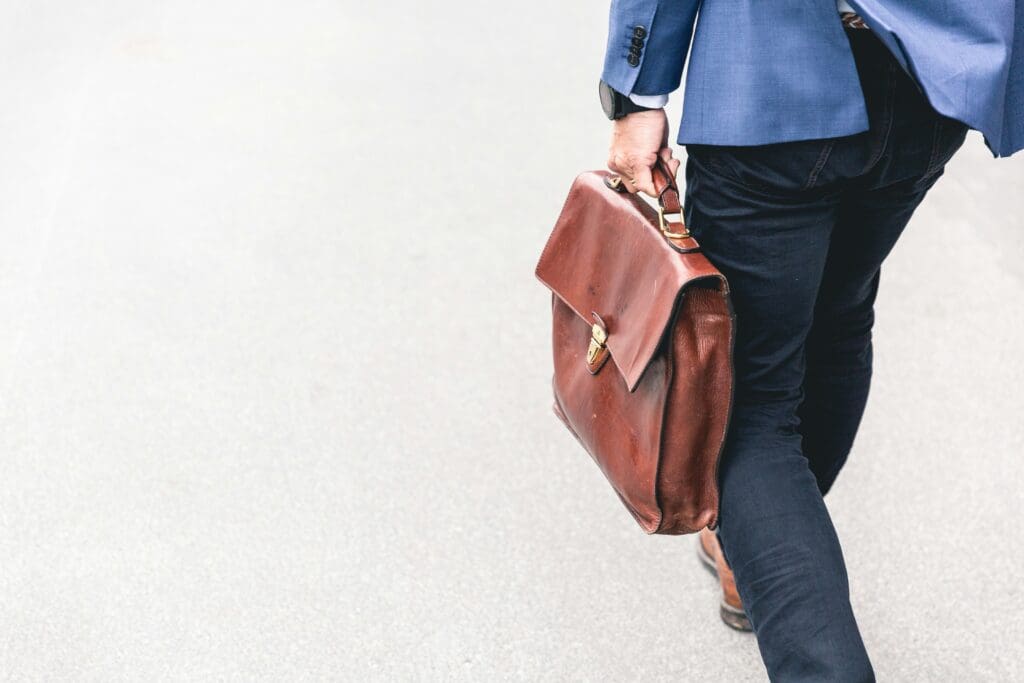 Man in jeans and blazer carrying a brown briefcase