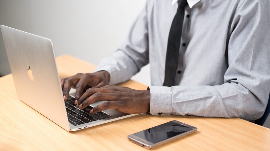 Man in button-down shirt with mobile phone typing on laptop computer