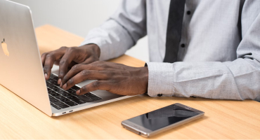 Man in button-down shirt with mobile phone typing on laptop computer