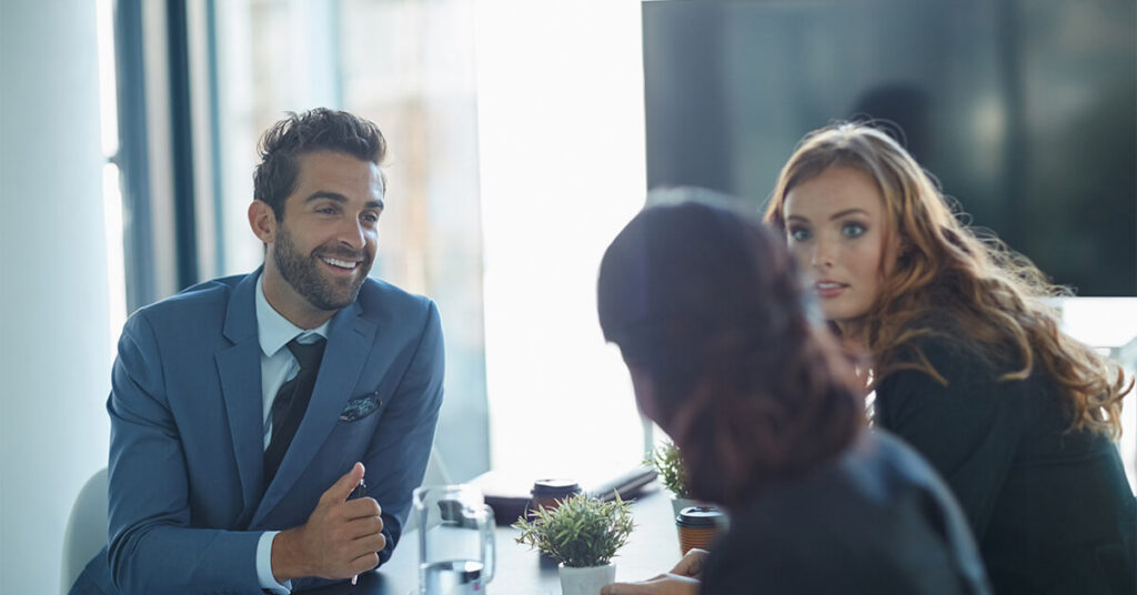 Two women and a man in business suits having a discussion in a conference room